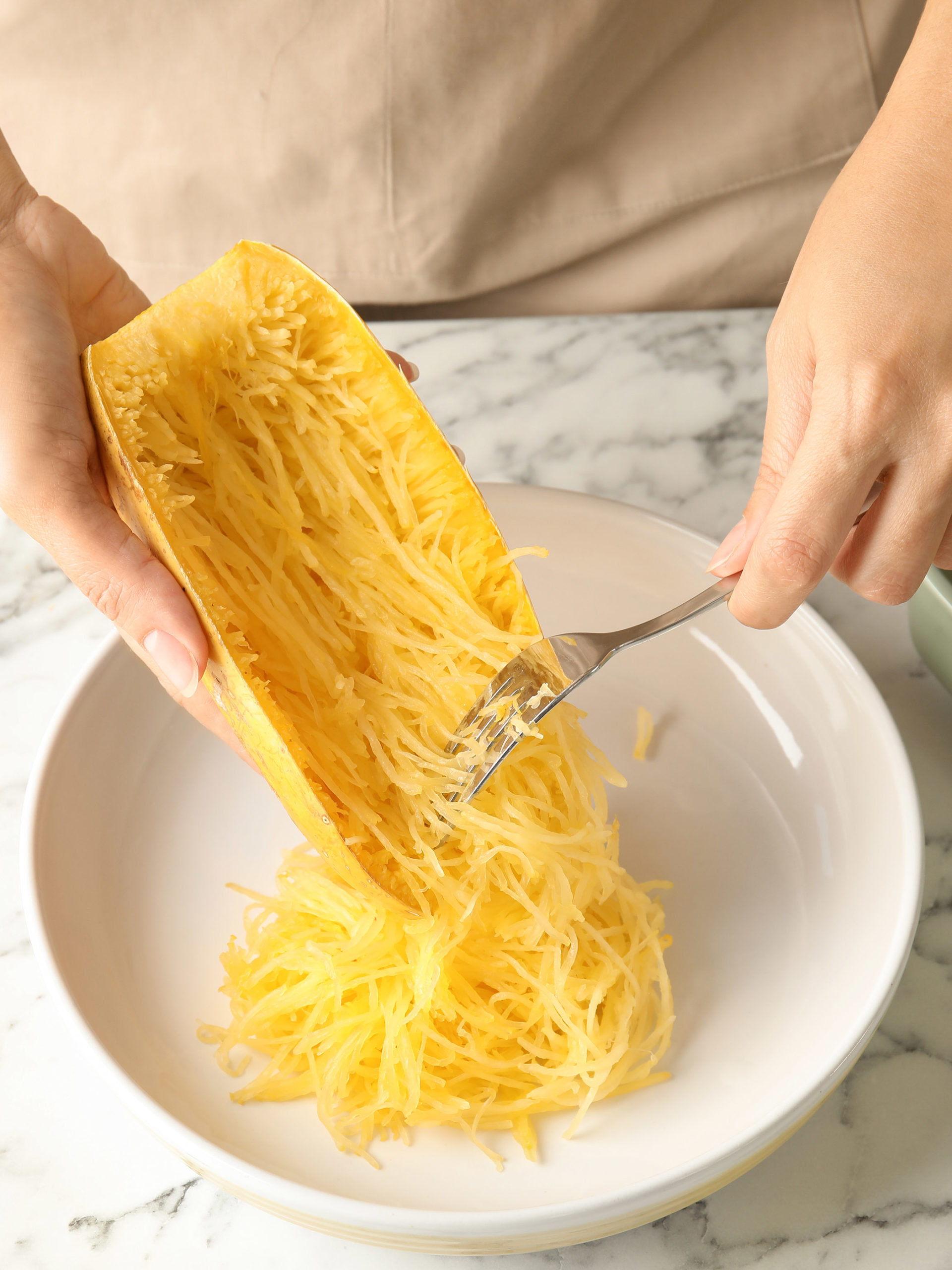 Woman scraping flesh of cooked spaghetti squash with fork in kitchen