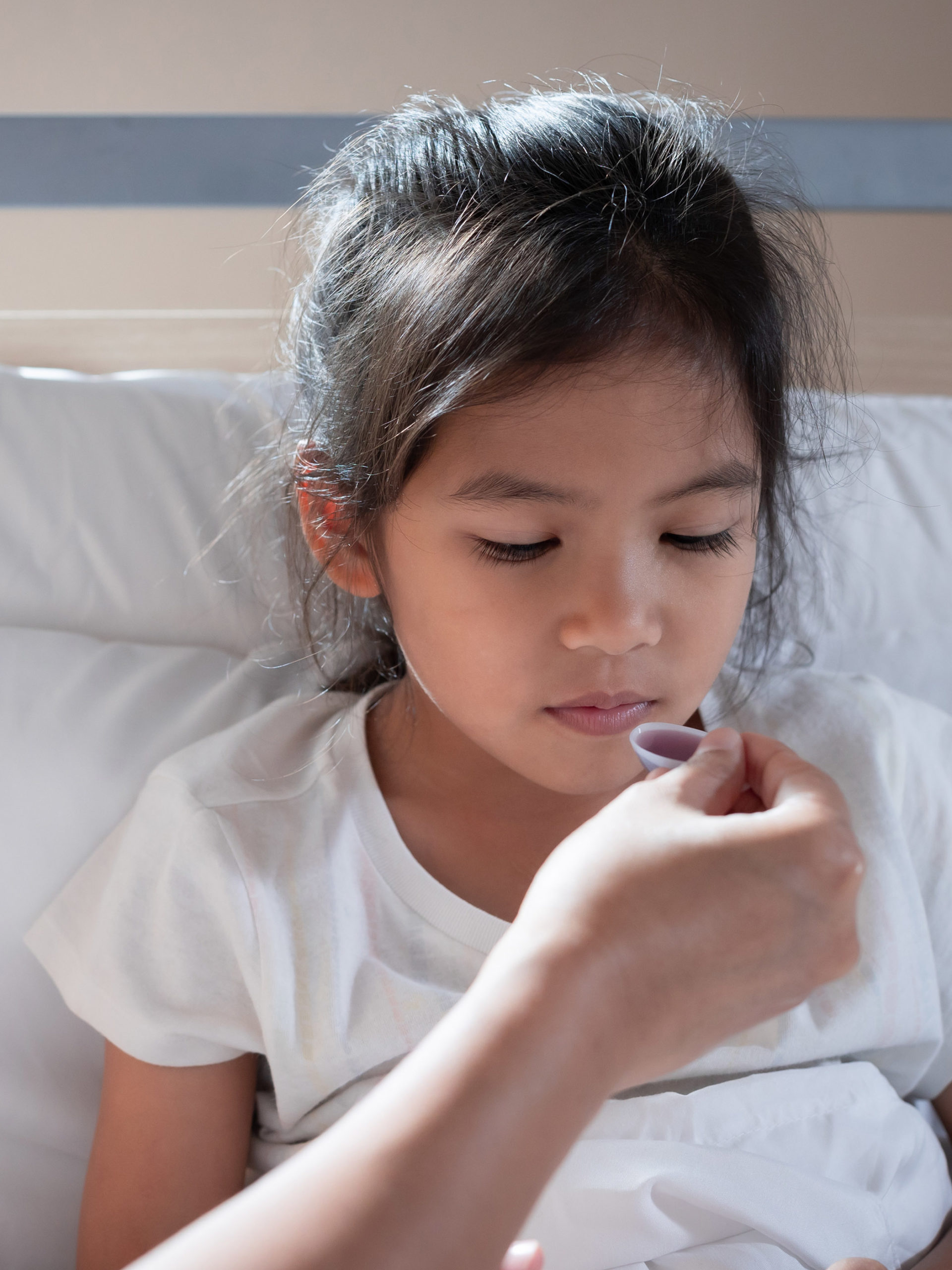 mother giving cough syrup medicine on a spoon to her daughter